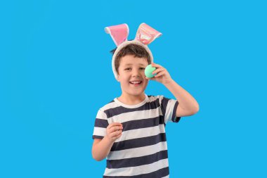Cute little boy with bunny ears and Easter egg on light blue background