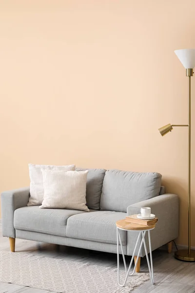 Grey sofa with cushions, lamp and table near beige wall