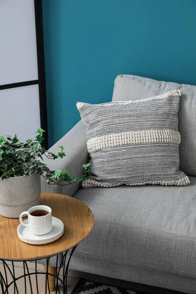 蓝色墙壁附近的灰色沙发 桌子上有软垫和一杯咖啡 — 图库照片
