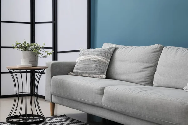 クッション付きのグレーのソファ テーブルの上の観葉植物と青い壁の近くの屏風 — ストック写真