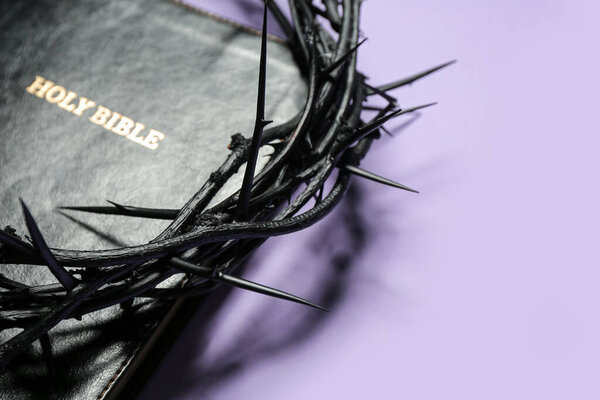 Crown of thorns and Holy Bible on lilac background, closeup