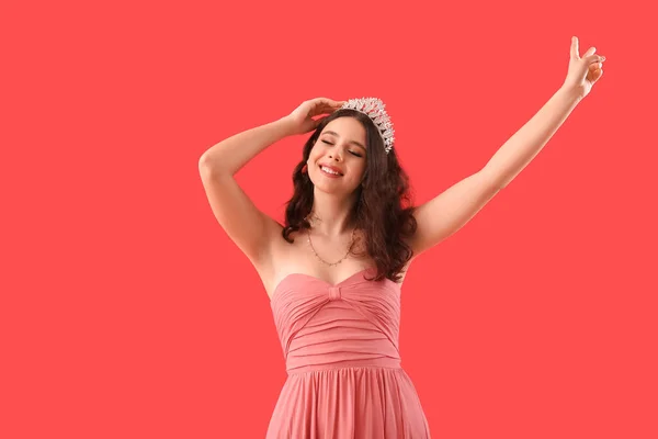 Teenage girl in tiara and prom dress on red background