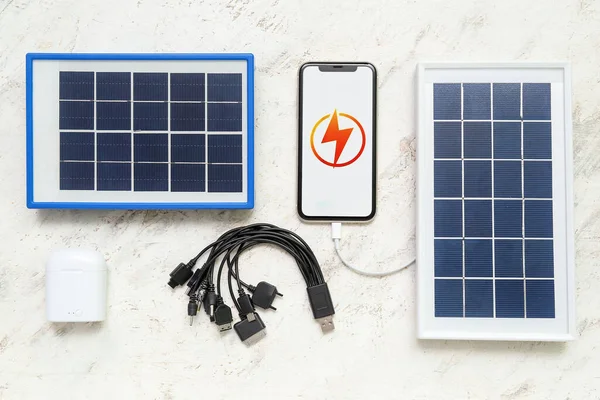Portable solar panels, mobile phone, wireless earphones and cables on white grunge background