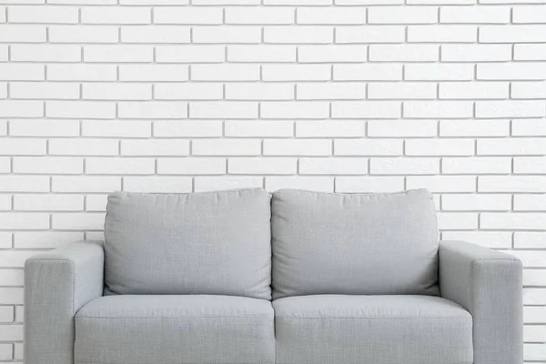 白いレンガの壁に近いスタイリッシュなグレーのソファ — ストック写真
