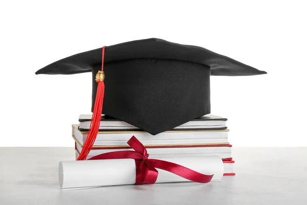stock image Graduation hat with diploma and books on table against white background