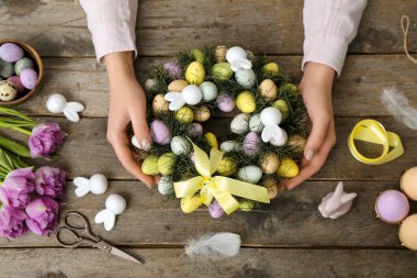 Woman making Easter wreath on wooden table, top view