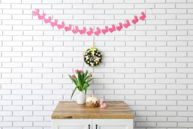 Vazoda laleler, Paskalya pastası, beyaz tuğla duvarda tavşan ve çelenk.