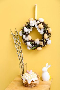 Vazoda söğüt dalları, Paskalya pastası, sarı duvarda tavşan ve çelenk olan masa.