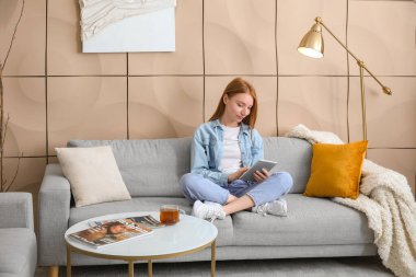 Evdeki gri koltukta tablet bilgisayar kullanan güzel bir kadın.