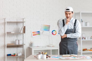 Masanın yanında düşünceli bir erkek ressam var.