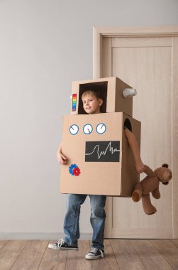 Işık duvarının yanında oyuncağı olan kartondan robot kostümlü küçük çocuk.