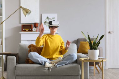 VR gözlüklü güzel bir kadın evdeki kanepede oturuyor.