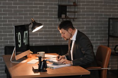 Male accountant working with calculator in office at night