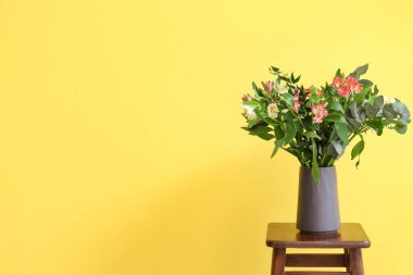 Sarı duvarın yanındaki taburede güzel alstromerya çiçekleri olan vazo.