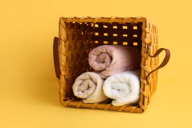 Sarı arka planda yumuşak havlular olan hasır sepet.