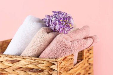 Katlanmış yumuşak havlular ve pembe arka planda sümbül çiçekli hasır sepet.
