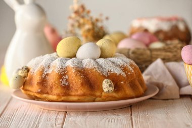 Plate with tasty Easter cake and painted eggs on white wooden table