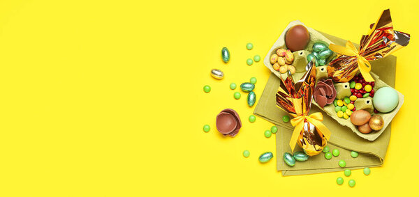 Chocolate Easter eggs and candies on yellow background with space for text