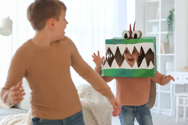 Little girl in cardboard dinosaur costume playing with her brother at home