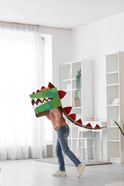 Little girl in cardboard dinosaur costume playing at home