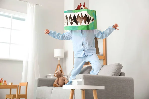 Little boy in cardboard dinosaur costume playing at home