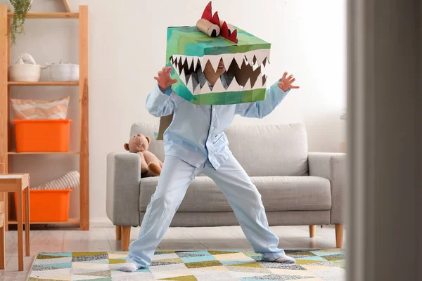 Little boy in cardboard dinosaur costume playing at home