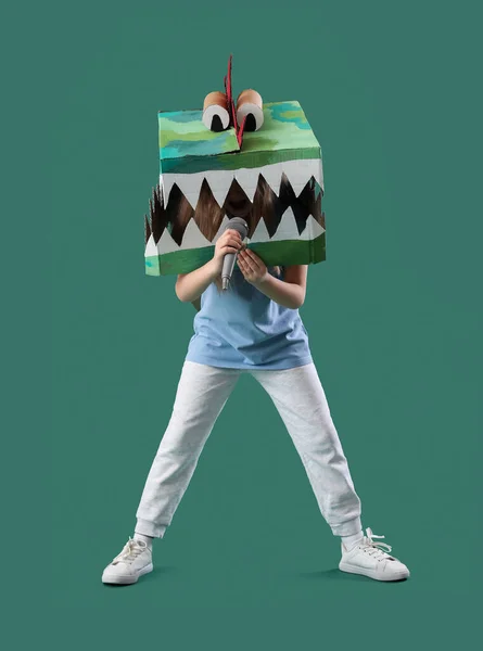 Little girl in cardboard dinosaur costume with microphone on green background