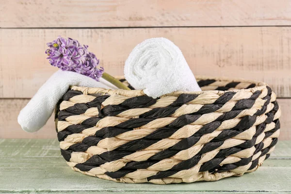 Stock image Basket with rolled soft towels and hyacinth flower on green wooden table