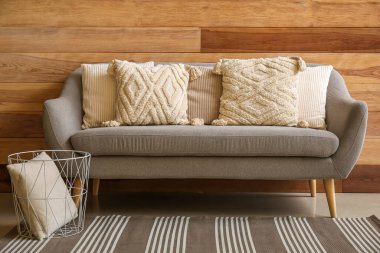 Ahşap duvarın yanındaki rahat gri koltukta şık dekoratif yastıklar.