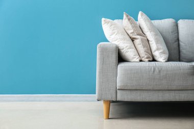 Stylish decorative pillows on cozy grey sofa near blue wall