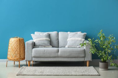 Stylish decorative pillows on cozy grey sofa near blue wall