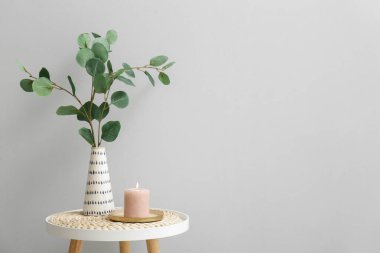 Okaliptüs dallarıyla yanan mum ve vazo gri duvarın yanındaki masada.