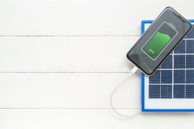 Portable solar panel charging mobile phone on white wooden background
