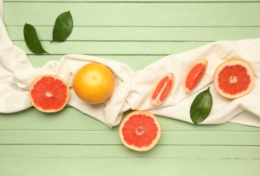 Olgun greyfurtlar, peçete ve bitki yapraklarıyla renklendirilmiş ahşap zemin üzerinde kompozisyon