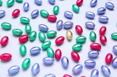 Açık arkaplanda renkli folyoyla çikolatalı Paskalya yumurtaları.