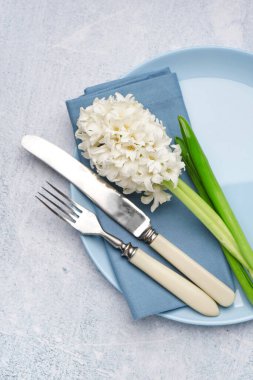 Çatal bıçaklı temiz tabak ve gri arka planda güzel bir sümbül çiçeği.
