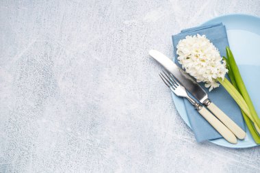 Çatal bıçaklı temiz tabak ve gri arka planda güzel bir sümbül çiçeği.