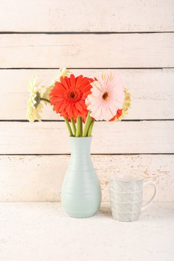 Beyaz ahşap duvarın yanındaki masada güzel Gerbera çiçekli vazo.