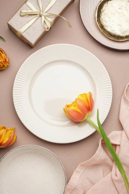 Temiz tabaklar, lale çiçeği ve bej arka planda çatal bıçak takımı.
