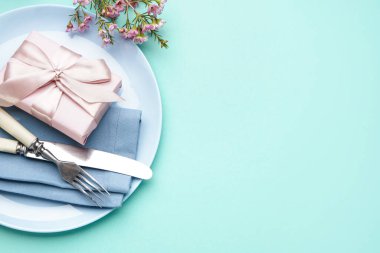 Hediye kutusu, çatal bıçak takımı ve turkuaz arka planda çiçek dekoru olan masa ayarı
