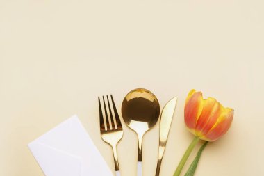 Çatal bıçak takımı, güzel lale çiçeği ve bej arka planda bir zarf.