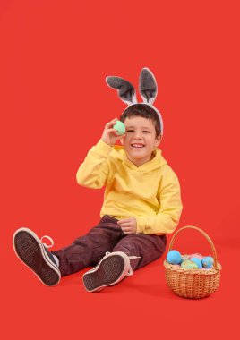 Cute little boy with bunny ears and Easter basket on red background