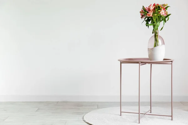 Vase with alstroemeria flowers on table near light wall