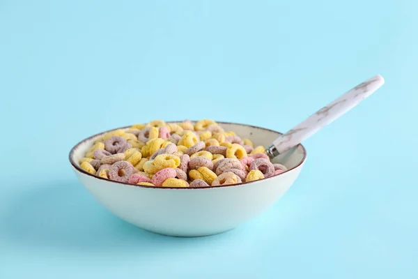 Bowl of colorful cereal rings with spoon on blue background