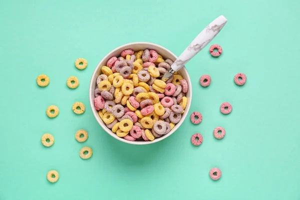Bowl of colorful cereal rings and spoon on turquoise background