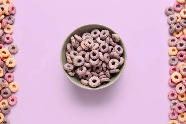 Bowl and heaps of colorful cereal rings on lilac background