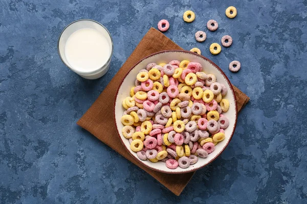 Bowl with colorful cereal rings and glass of milk on blue grunge background