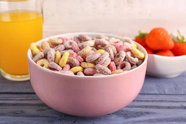 Bowl with colorful cereal rings, glass of juice and strawberries on blue wooden table