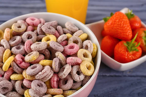 Bowl with colorful cereal rings and strawberries on blue wooden table