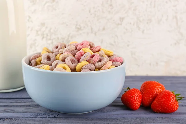 Bowl with colorful cereal rings and strawberries on blue wooden table near white grunge wall
